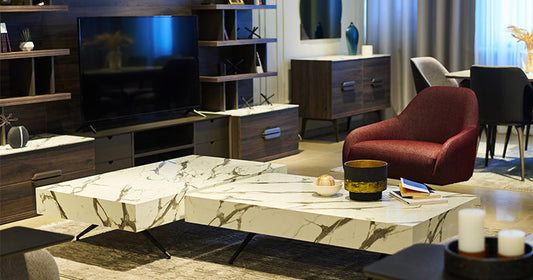 Luxurious living room interior with contemporary marble coffee tables, dark wood shelves, and a textured red accent chair.