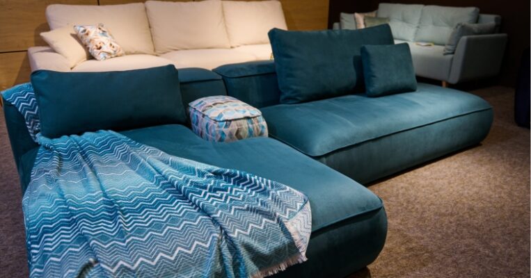 L-shaped fabric lounge with dark brown armrests placed in a living room with wooden flooring
